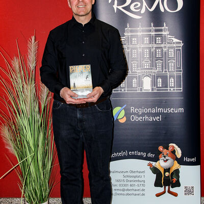 Tim Pieper mit seinem Buch in der Hand vor dem Banner des ReMO - Regionalmuseum Oberhavel