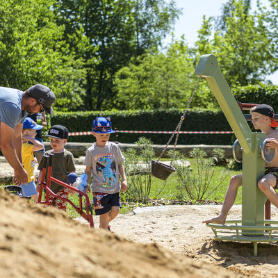 Kinder spielen auf einem Spielplatz unter Aufsicht eines erwachsenen Mannes.