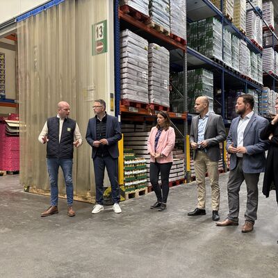 Vier M&auml;nner und zwei Frauen mittleren Alters stehen im Halbkreis in einem Warenlager.