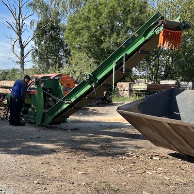 Ein Mann im Blaumann mit Schallschutzkopfh&ouml;rern bedient eine landwirtschaftliche Anlage, in der Baumst&auml;mme zu Kamin- und Brennholz verarbeitet werden.