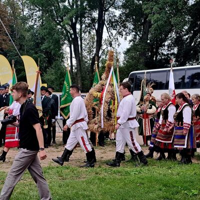 M&auml;nner und Frauen in traditioneller, polnischer Tracht laufen &uuml;ber eine Wiese. Im Hintergrund ein wei&szlig;er Reisebus.