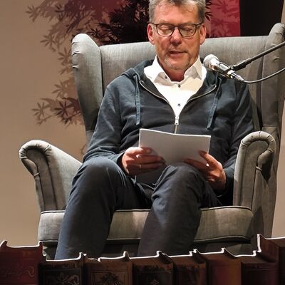 Autor Richard Brandes sitzt in einem Sessel auf der B&uuml;hne und liest aus seinem Krimi "Gejagt durch Brandenburg"