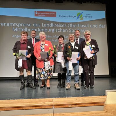 Mehrere M&auml;nner und Frauen mit Urkunden in den H&auml;nden auf einer kleinen Theaterb&uuml;hne.