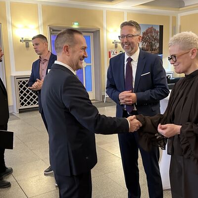 M&auml;nner und eine Frau auf einem Stehempfang bei einer Begr&uuml;&szlig;ung.