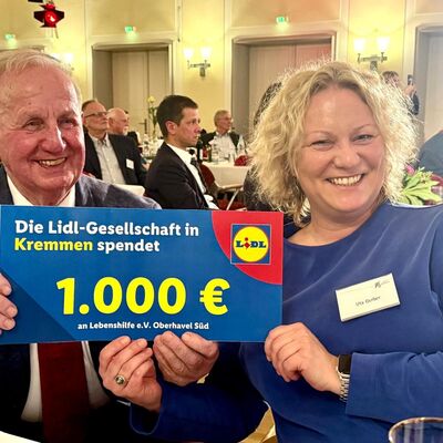 Ein Mann und eine Frau halten einen symbolischen Spendenscheck der Lidl-Gesellschaft &uuml;ber 1.000 Euro in die Kamera.