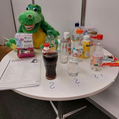 Ein wei&szlig;er runder Tisch mit einem gr&uuml;nen Pl&uuml;schkrokodil und Getr&auml;nkenachbildungen f&uuml;r die Zuckerausstellung.