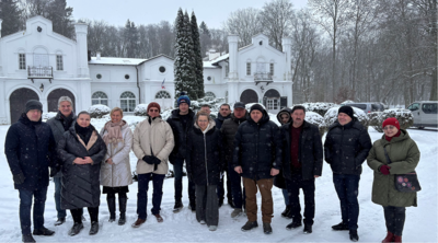 Eine Gruppe von M&auml;nnern und Frauen steht in einer schneebedeckten Landschaft vor einem wei&szlig;en Geb&auml;ude. 
