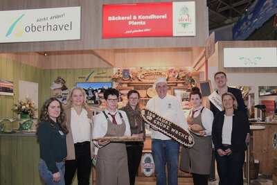 Eine Gruppe von Frauen und M&auml;nnern stehen vor einem Messestand auf der Gr&uuml;nen Woche.