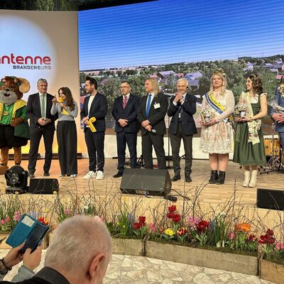 Eine Delegation aus M&auml;nnern und Frauen steht auf einer B&uuml;hne auf der Gr&uuml;nen Woche 2026 des Radiosenders Antenne Brandenburg.